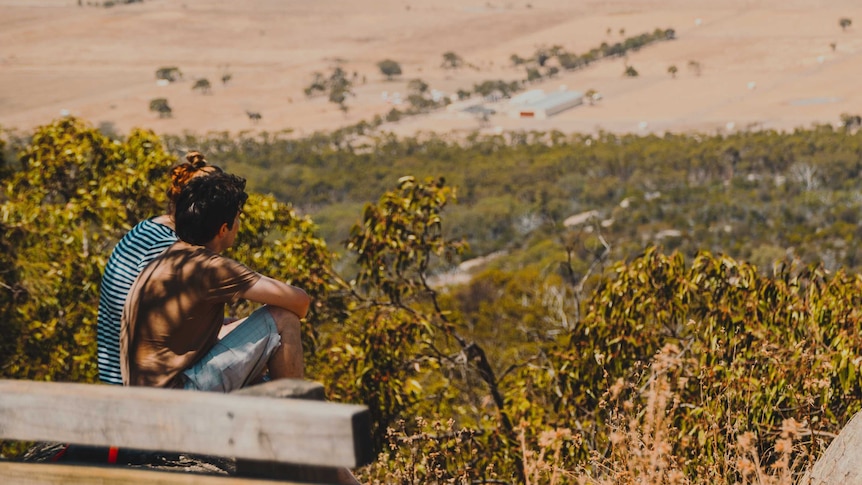 Two teenagers sitting on a hill overlooking a landscape below