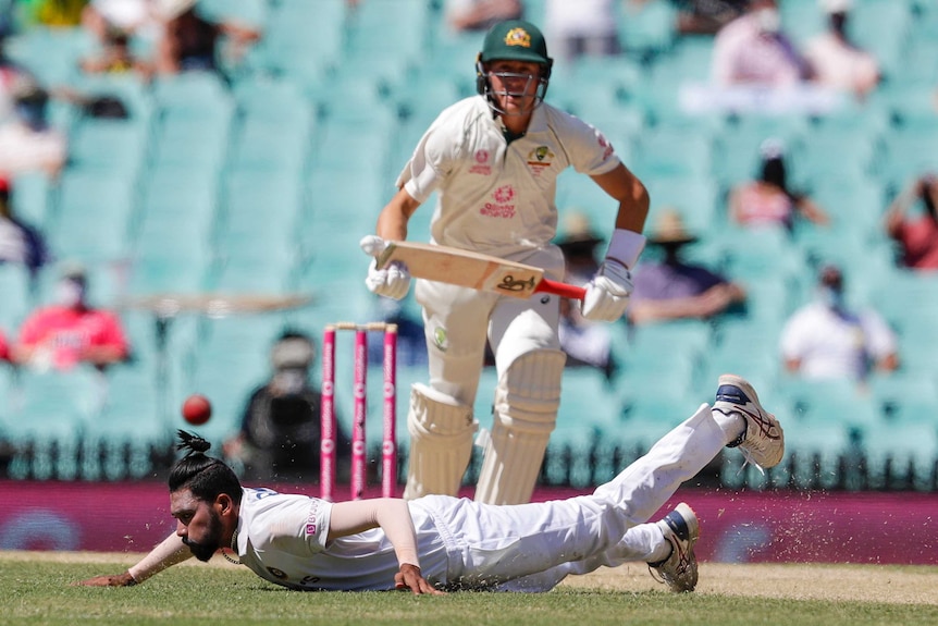 Mohammed Siraj dives onto his stomach to try to stop a ball. Marnus Labuschagne prepares to run