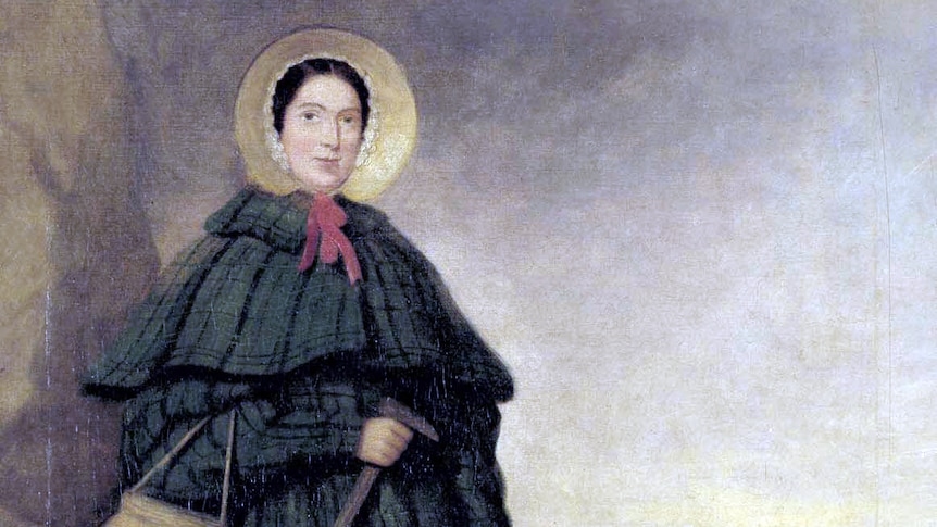 A portrait of Mary Anning wearing a cloak, bonnet and carrying a pick and basket while standing on the beach.