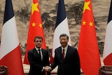 Emmanuel Macron and Xi Jinping shake hands as the pose for a photo in front of French and Chinese flags.