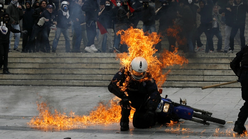 A policeman is seen in flames as he tries to escape after a petrol bomb was thrown at him during riots in Greece