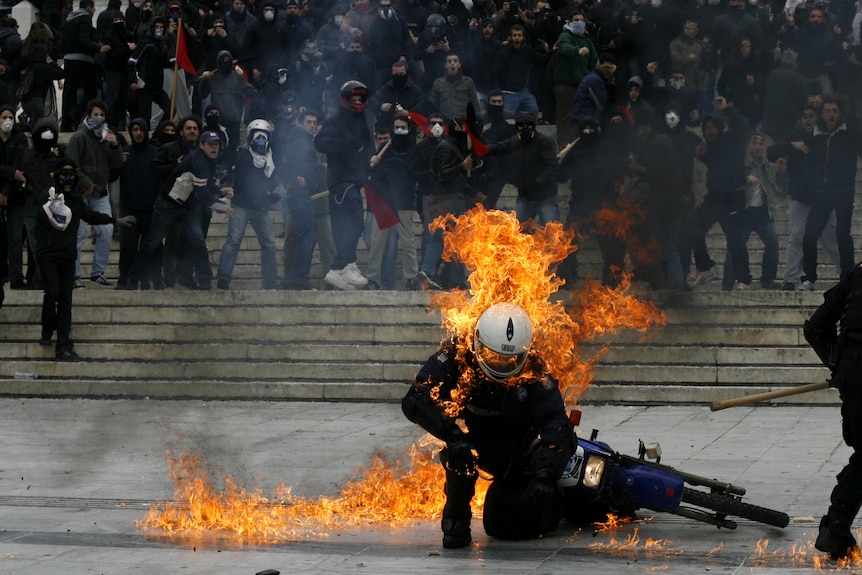 A policeman is seen in flames as he tries to escape after a petrol bomb was thrown at him during riots in Greece