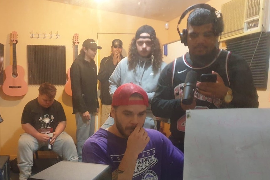 Five young men sit behind Tasman Keith, who is working on a computer screen in a recording studio