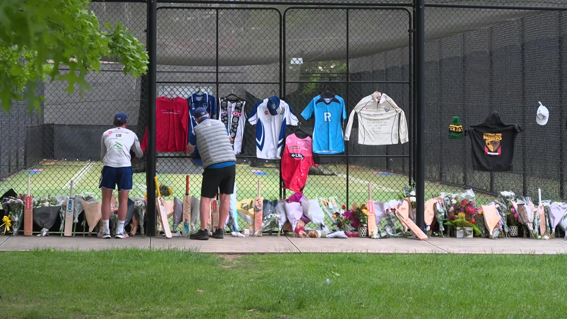 Two men laying tributes against cricket nets