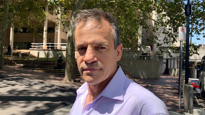 A grey haired man standing in a leafy street