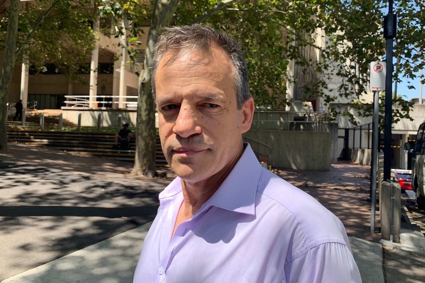 A grey haired man standing in a leafy street