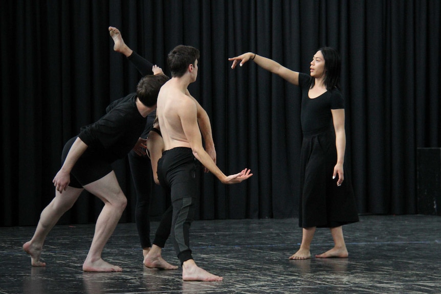 A woman choreographs a group of dancers.