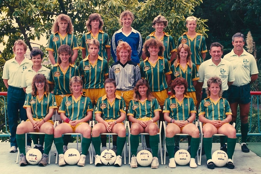 A women's soccer team wearing green and yellow uniforms poses for a photo