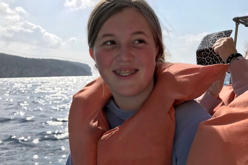 Kate smiles on a boat wearing a life jacket, there is water behind her.