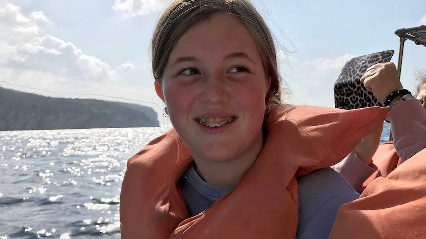 Kate smiles on a boat wearing a life jacket, there is water behind her.