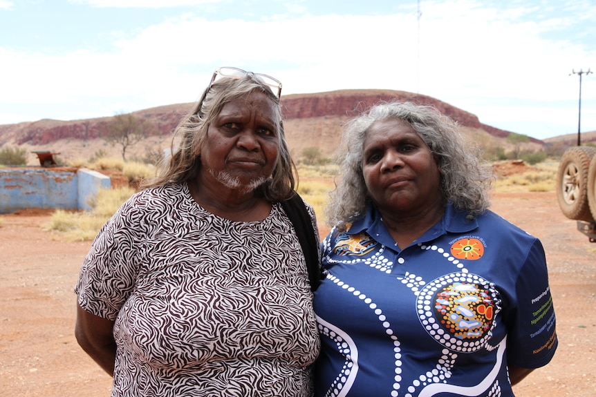 The pair stand together near a large escarpment