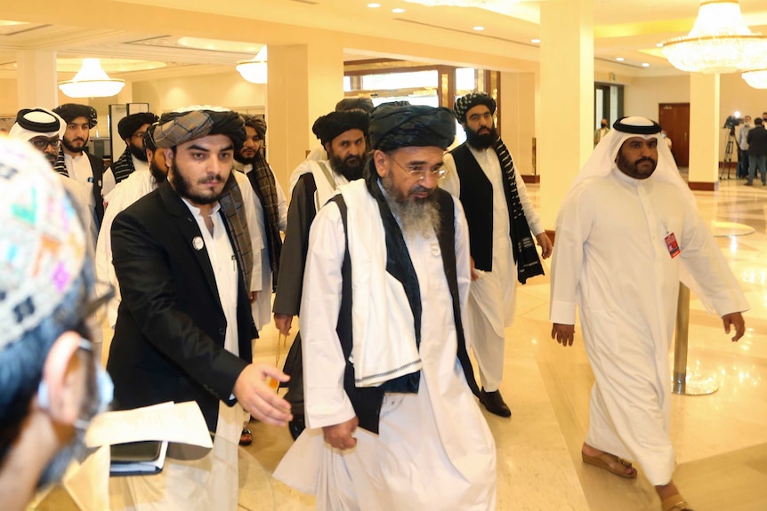 A group of men wearing traditional Afghan clothing walk through a brightly lit lobby.