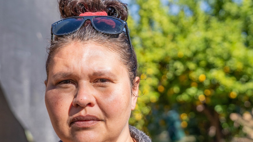 A woman with sunglasses on her head, looking serious, outside on a sunny day.