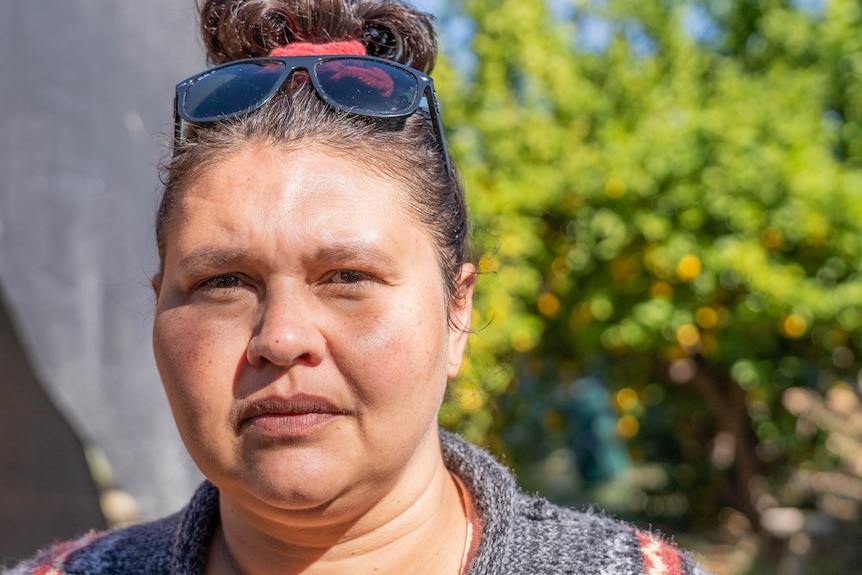 A woman with sunglasses on her head, looking serious, outside on a sunny day.