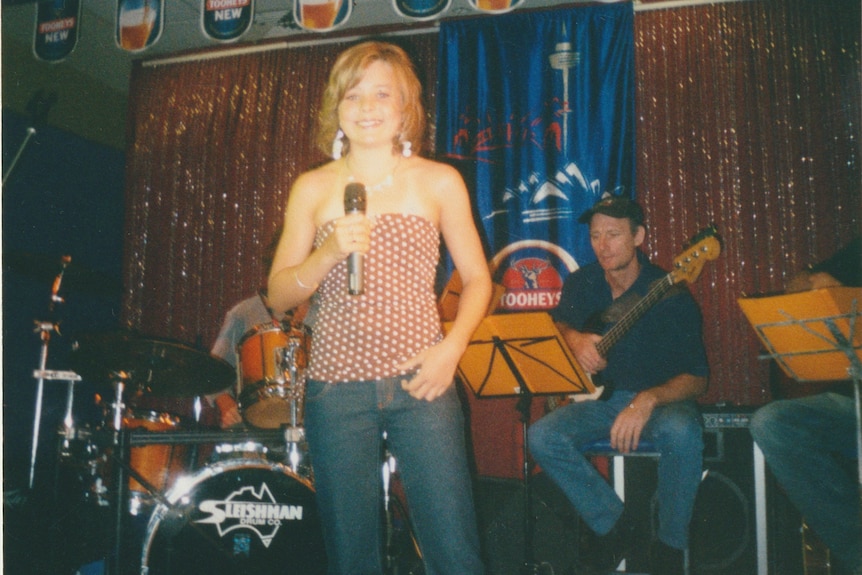 A young girl on stage with a band, holding a microphone