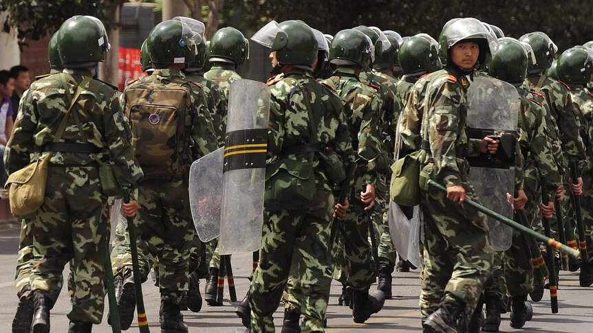 Soldiers wearing helmets and holding batons walk on the streets