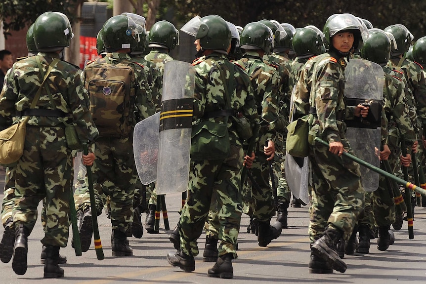 Soldiers wearing helmets and holding batons walk on the streets