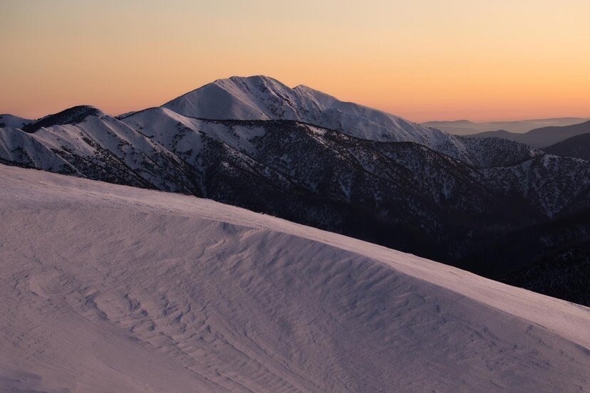 An orange sun sets behind a snow covered alpine horizon. 