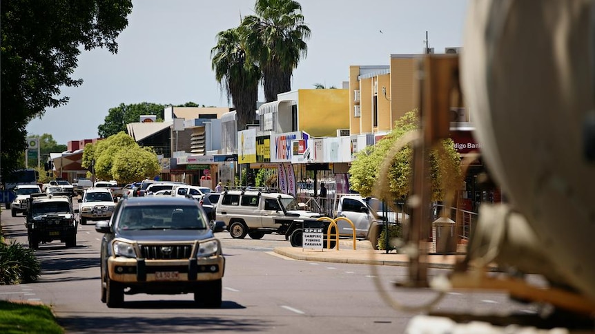 Rue principale d'une ville de campagne, avec un 4x4 au premier plan et des palmiers.