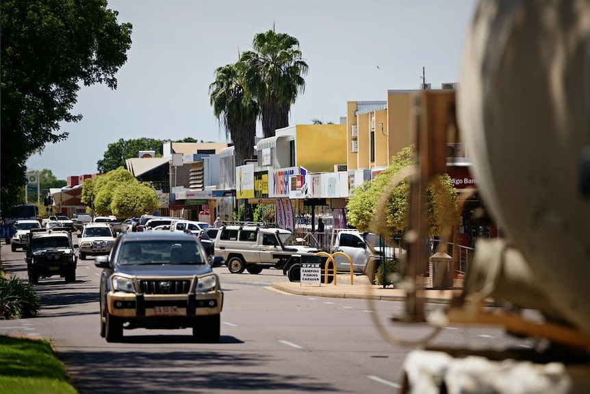 A country town main street, with a four-wheel drive in the foreground and palm trees.