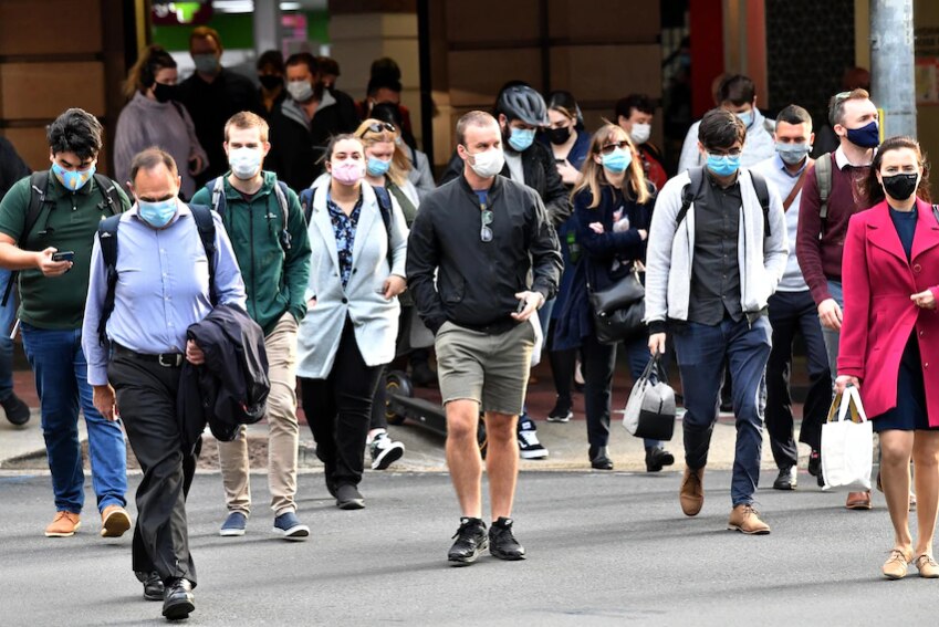 A group of people cross the street, all wearing masks.