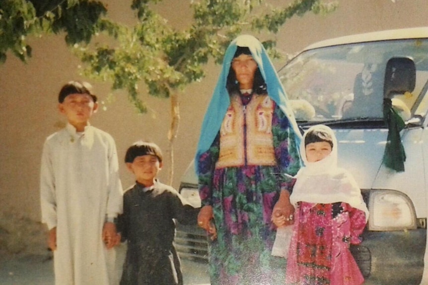 Two young boys and a young girl stand with an older woman