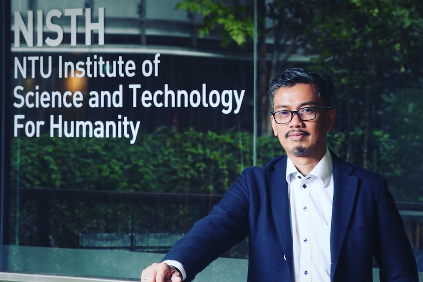 Man wearing suit and glasses facing the camera in front of the NTU Institute of Science and Technology sign.