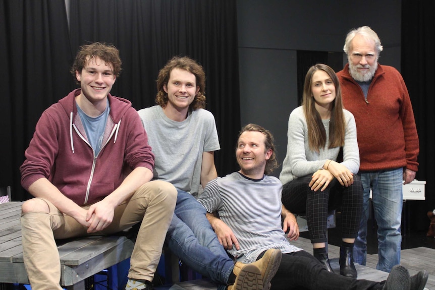 Some of the cast sitting on the stage at a rehearsal.