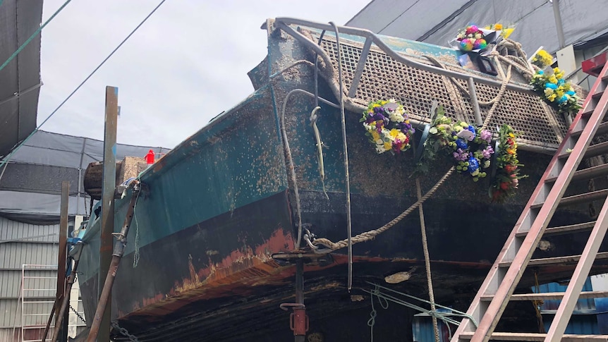Flower wreaths on the stern of salvaged boat on a gantry in a marina