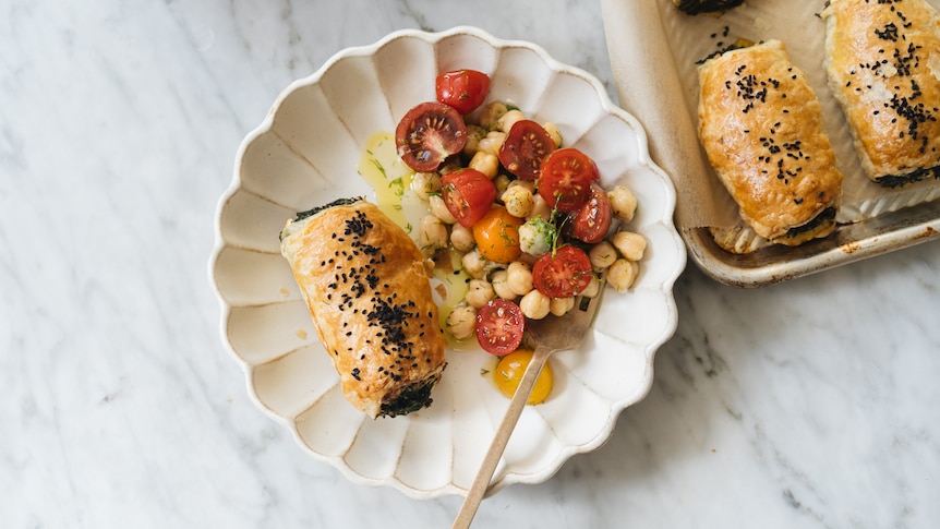 A baked pastry roll served on a plate with tomato, chickpea and dill salad.