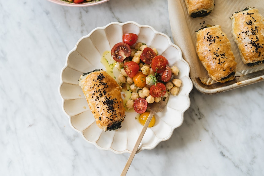 A baked pastry roll served on a plate with tomato, chickpea and dill salad.