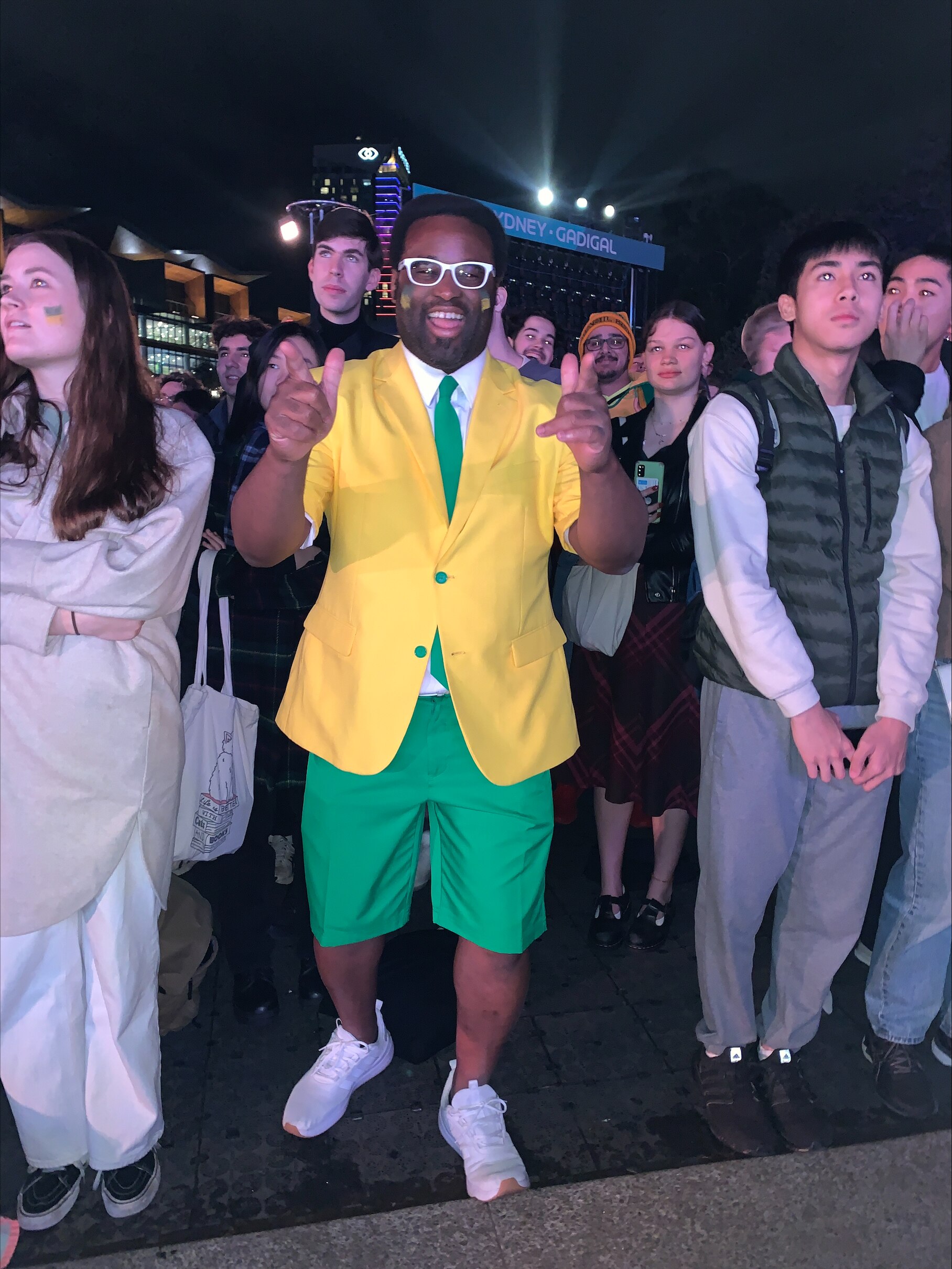 a man wearing white glasses pointing at the camera and smiling