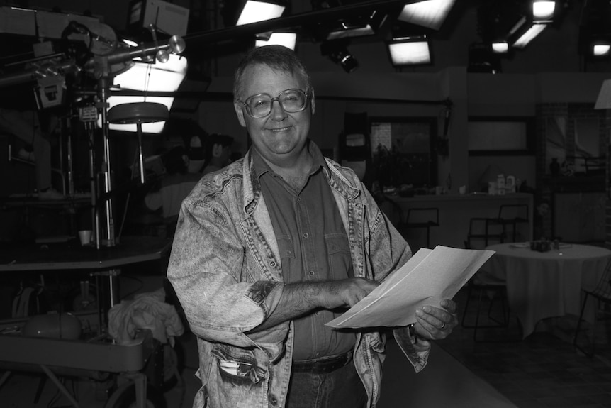 A black and white image of a man holding a script and smiling.