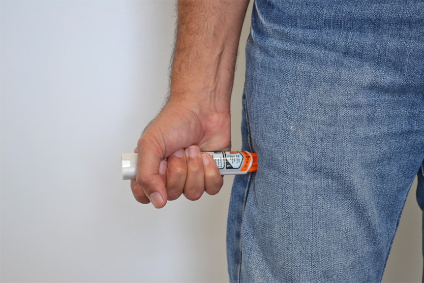 Epipen being held by a hand against a leg.