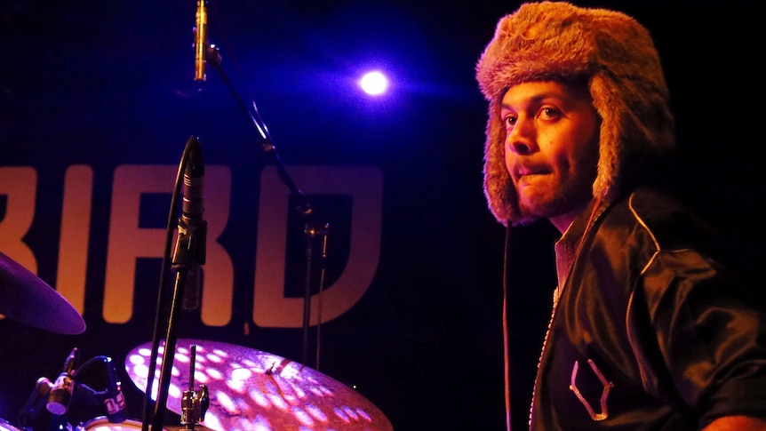 Yussef Dayes sits behind his drum kit, wearing a Russian-style hat