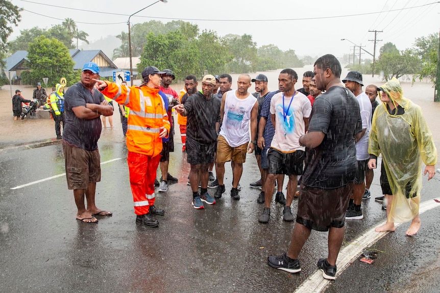 A group of Fijian men stand around a SES volunteer in floodwaters.