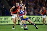 A young Western Bulldogs player turns his body to one side as he brings his fist back to handball during a game.