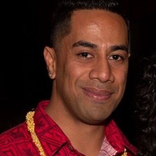 A man smiles while wearing Pacific Islander style red shirt