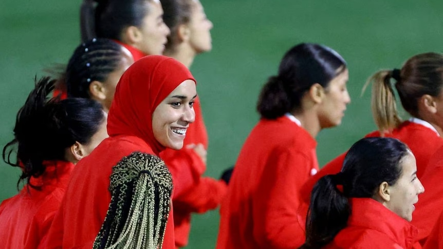 Women wearing red soccer jerseys walking onto a green pitch 