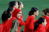 Women wearing red soccer jerseys walking onto a green pitch 