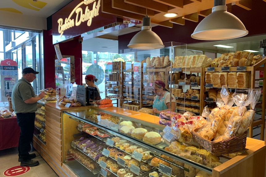 A man shops at a bakery with cashiers behind plastic shields.