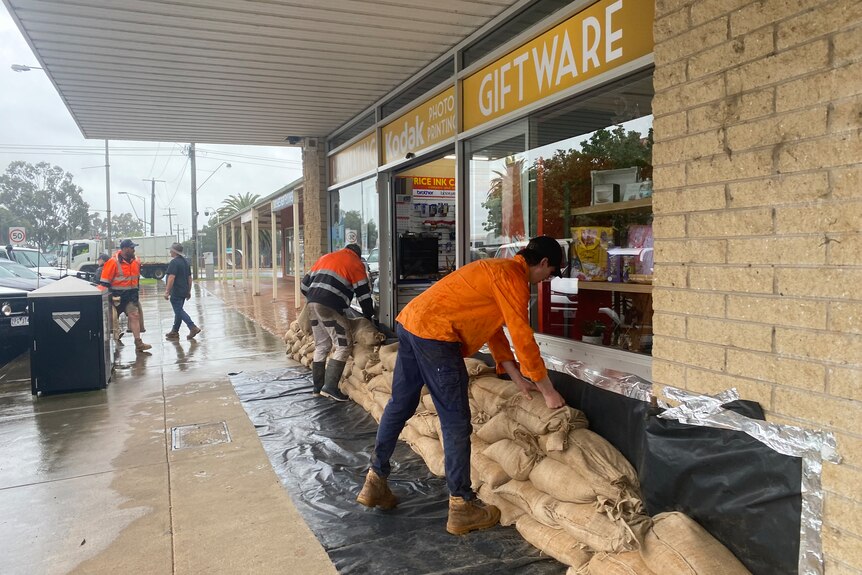 SES workers pule sandbags next to the windows of a shop. 