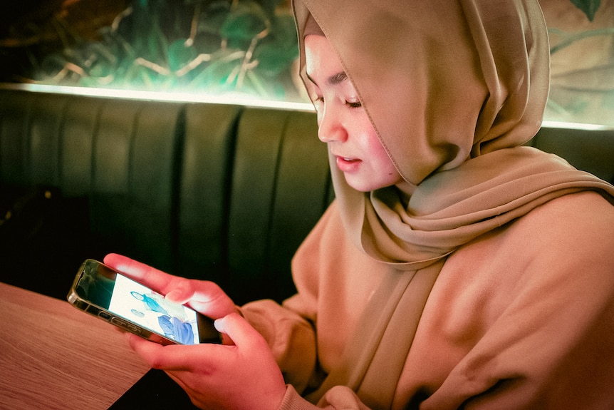 Adiba looks on her phone at photos of her family while sitting in a Melbourne cafe. 