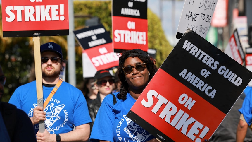 Writers and supporters holding up signs such as "Writers Guild of America on Strike!" and "It didn't have to be this way"