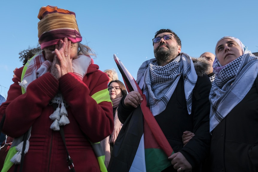 A woman crying while a man next to her holds a Palestinian flag