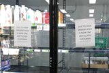 Milk fridges in a supermarket are almost empty with signs on the doors limiting customers to one bottle each