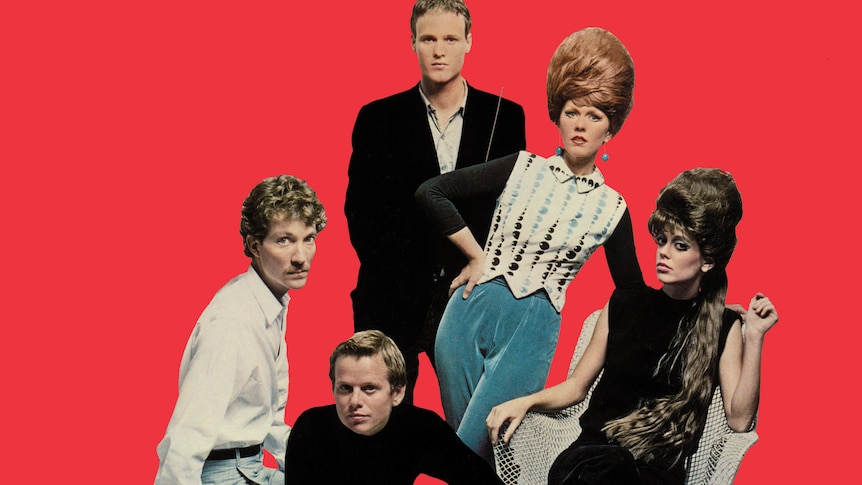 three men and two women wear vintage clothes before a bright red background. the women have tall bouffant hairstyles.