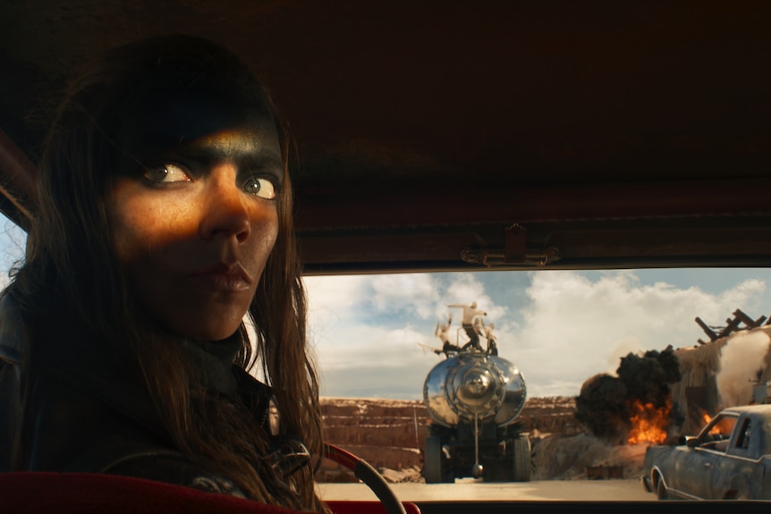 Film still of a woman, silhouetted with only her eyes glowing, looking over her shoulder in the cab of a truck.