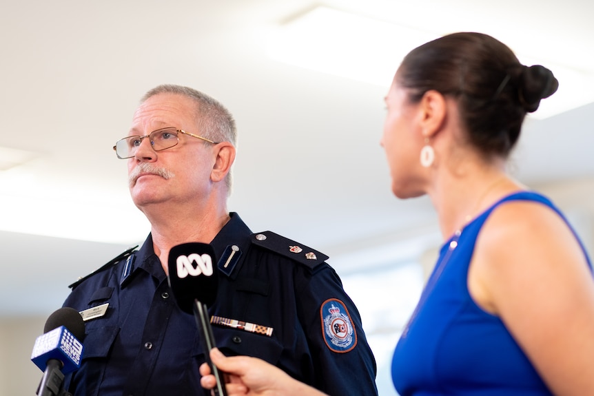 A man with a serious expression talks into two microphones. He is wearing a NTES uniform.