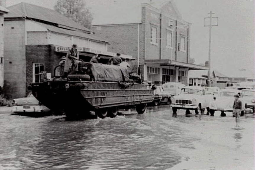 Soldiers in a boat with wheels drive up a flooded street.